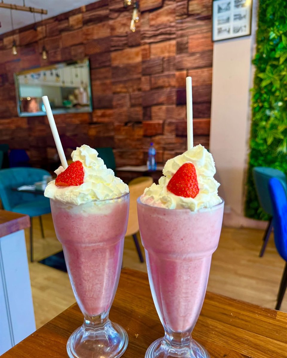 Two milkshakes topped with cream and strawberries